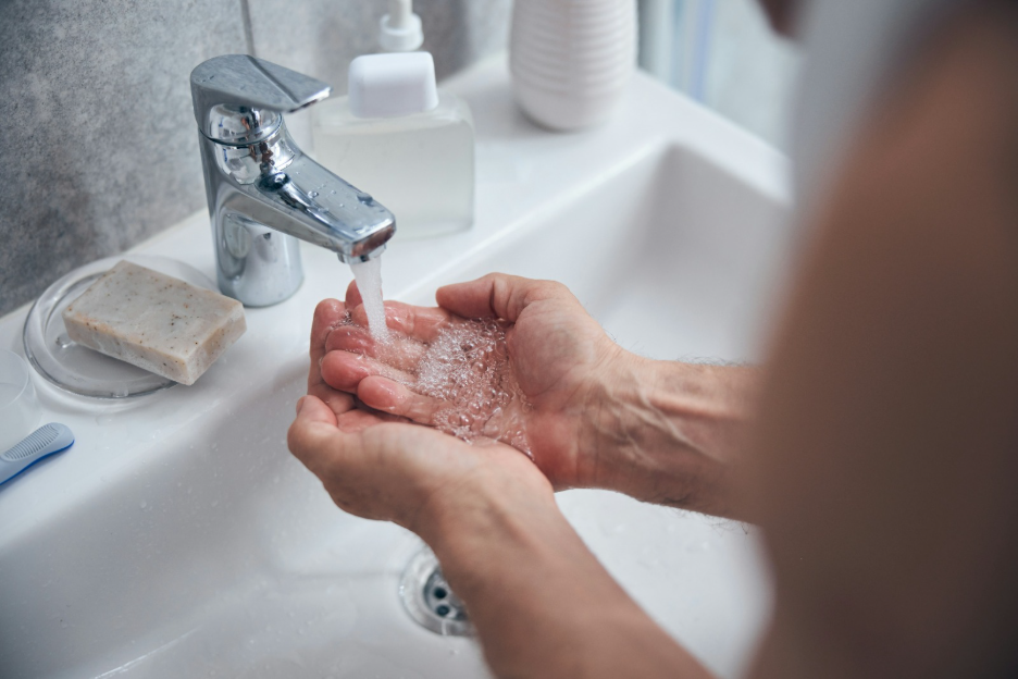 Elderly person washing hands at sink, a daily hygiene task often covered under bathing assistance