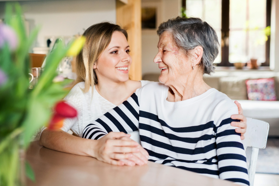 Family caregiver sitting with elderly mother at home, sharing a warm moment together